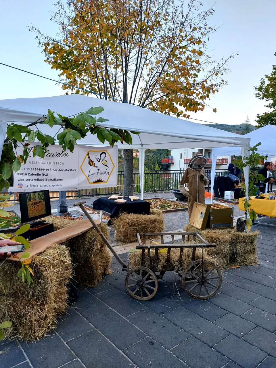 Lo stand La Favola alla sagra della castagna di Calvello, con balle di paglia, un carretto di legno e il manichino da apicoltore